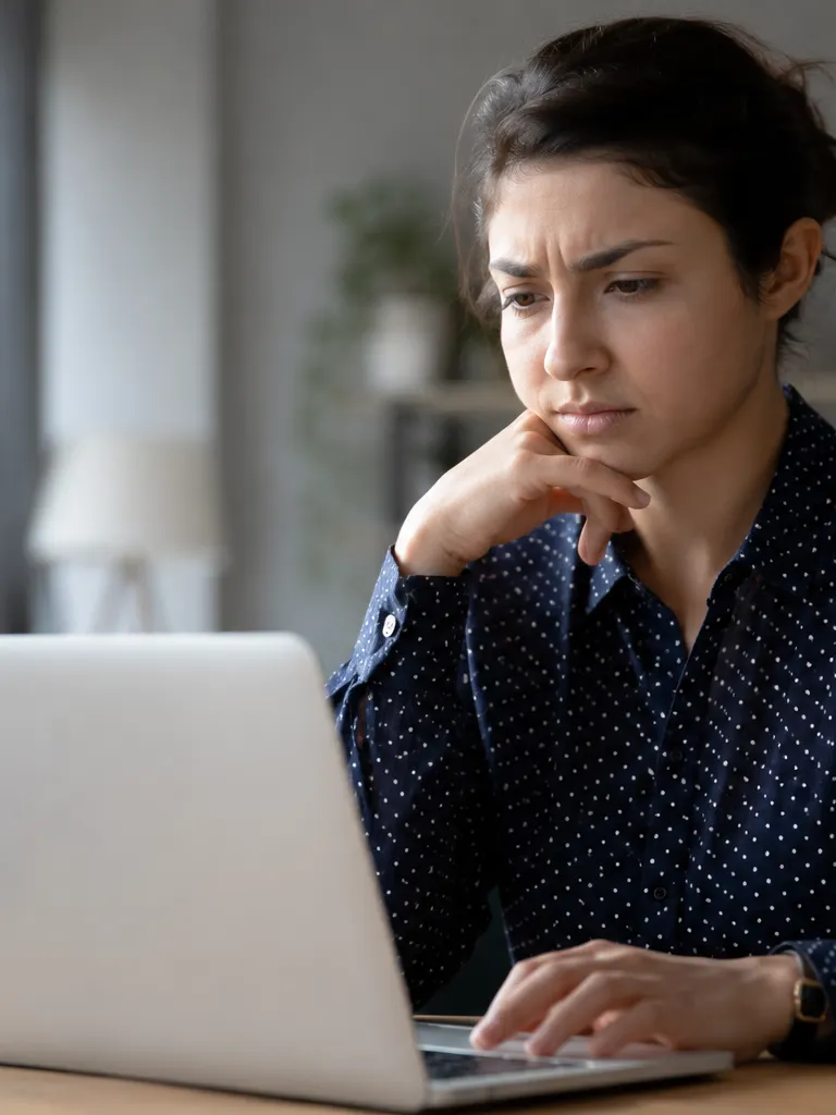 A woman sits at a desk reviewing her laptop with a concerned expression, reflecting the uncertainty job applicants face when an automated screening tool decides their application.